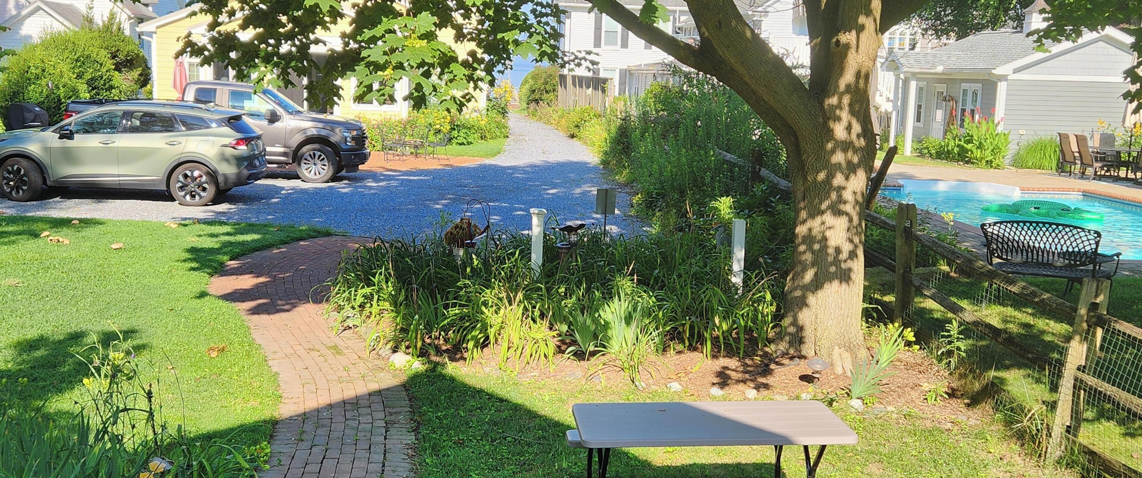 Een oprit met een geparkeerde auto, een tuin met een tafel en bank, en een zwembad.