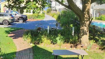 Een oprit met een geparkeerde auto, een tuin met een tafel en bank, en een zwembad.
