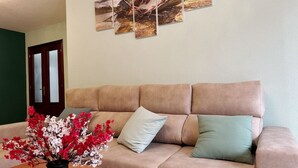 Una sala de estar con un sofá beige, un jarrón con flores rojas y blancas, y una mesa de centro de madera.