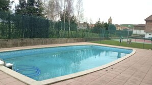 Una piscina rectangular con solárium empedrado, rodeada de una valla y vegetación.