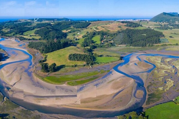 An aerial view of a coastal landscape with winding rivers, green fields, and a hill with a structure on top.