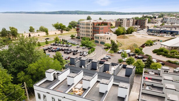 A modern building with a flat roof, large windows, and a parking lot in front. - BRAND NEW downtown TC rooftop condo skyline views (Traverse City)