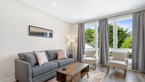 A modern living room with a grey sofa, a wooden coffee table, and a white armchair. - BRAND NEW downtown TC rooftop condo skyline views (Traverse City)