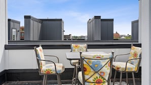 A rooftop terrace with four chairs and a table, overlooking a cityscape. - BRAND NEW downtown TC rooftop condo skyline views (Traverse City)