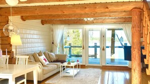 A cozy cabin interior with a wooden ceiling, a sofa, a dining table, and a staircase. - Log house with private beach and own dock incl. boat (Njurunda)