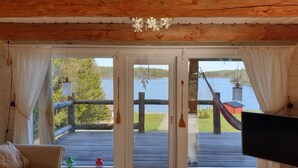 A cabin with a wooden interior, a TV, and a deck with a view of a lake and dock. - Log house with private beach and own dock incl. boat (Njurunda)