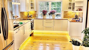 A spacious kitchen with wooden flooring, white cabinets, and a large window providing natural light. - Log house with private beach and own dock incl. boat (Njurunda)