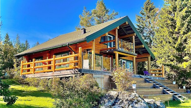 A log cabin with a wooden deck, a covered porch, and a stone foundation. - Log house with private beach and own dock incl. boat (Njurunda)