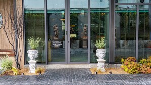 Fachada de un edificio con puerta de cristal, dos estatuas y plantas en macetas.