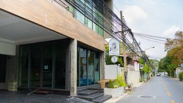 A hotel entrance with a modern design, including a glass facade, a wooden bench outside, and a clear road with a no parking sign.