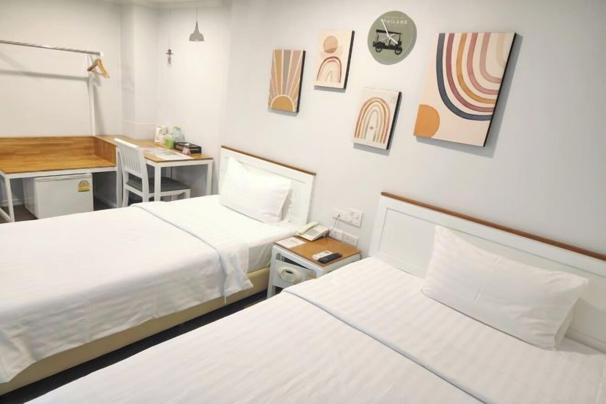 Habitación de hotel con dos camas, un escritorio y una silla. Hay obras de arte en la pared y un reloj.