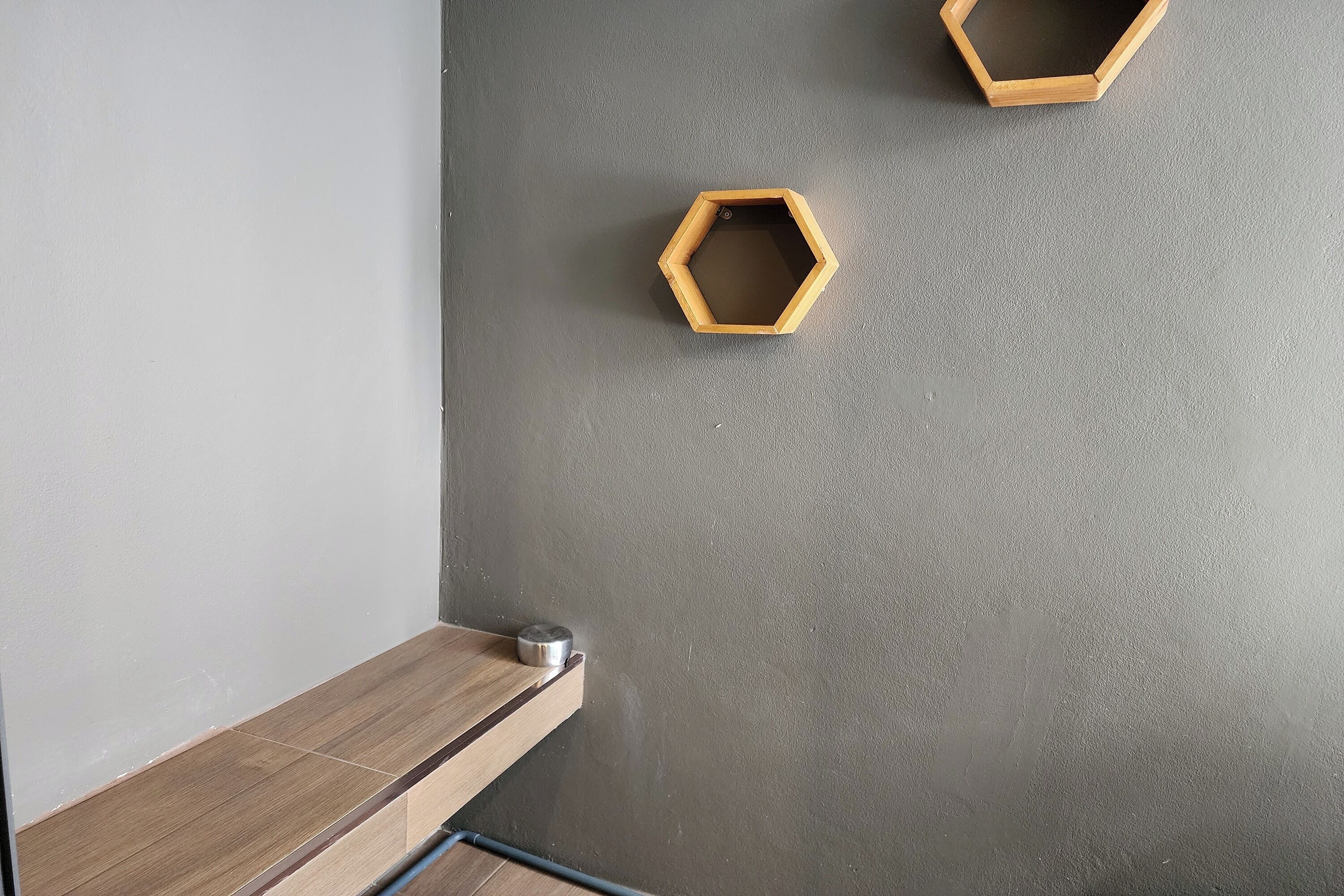 A room with a grey textured wall, a wooden shelf, and two hexagonal wooden shelves.