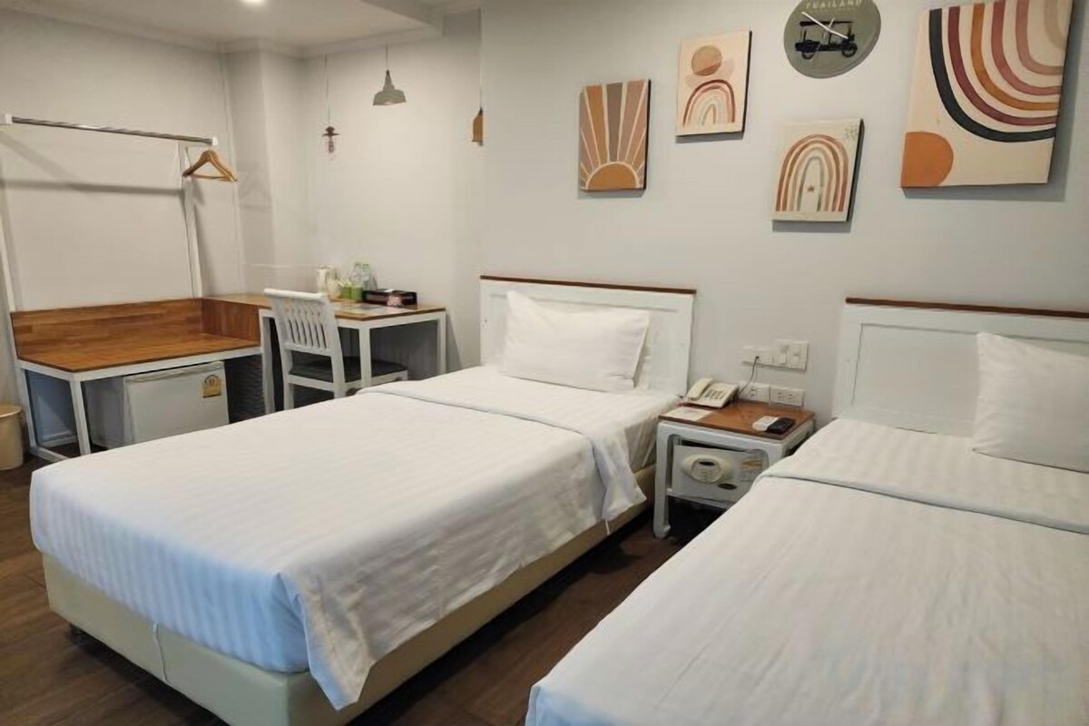 Quarto de hotel com duas camas, uma mesa de escritório, uma cadeira, mesa de cabeceira com telefone e relógio fixado na parede.