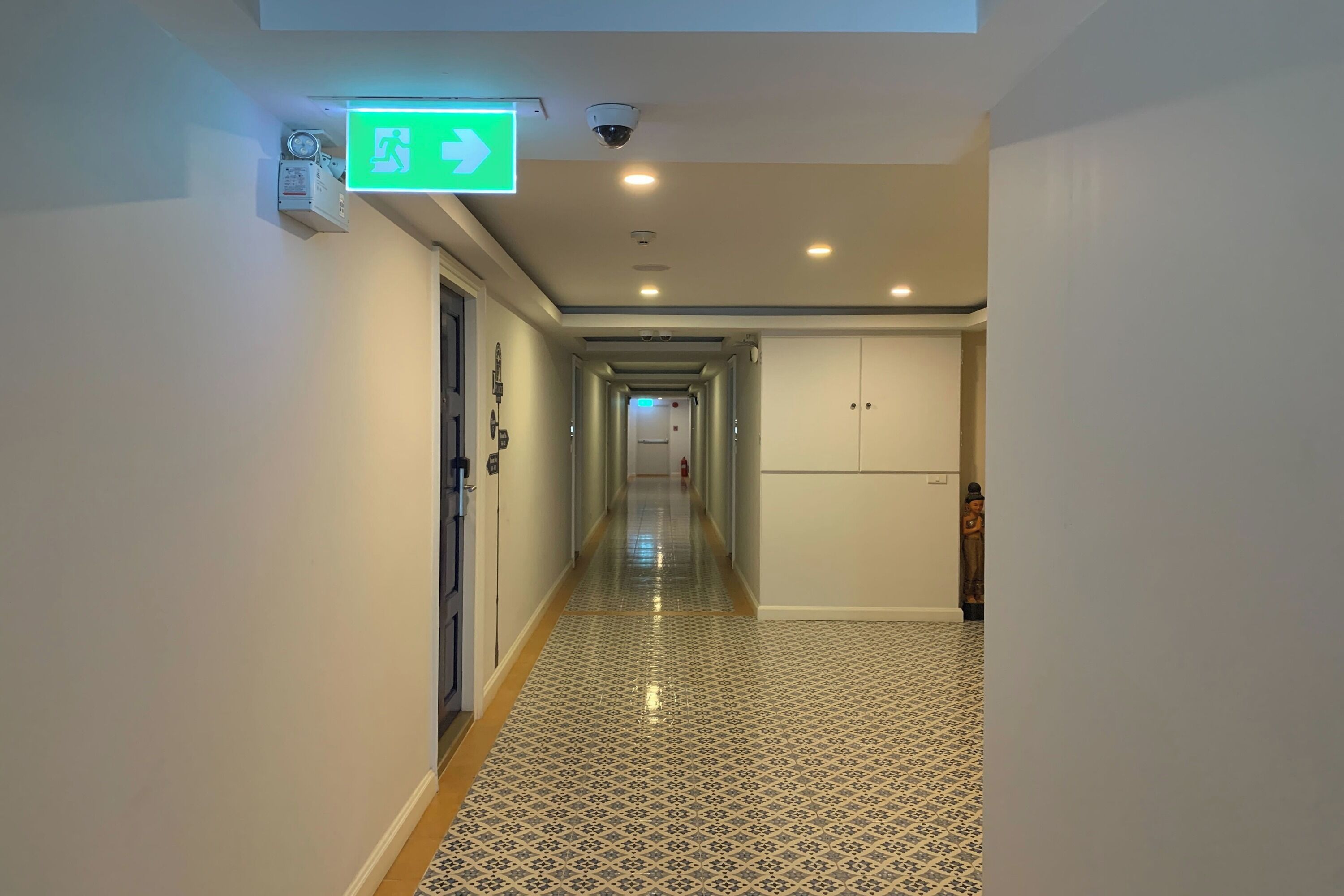 A hallway with patterned flooring, a green emergency exit sign, and a fire extinguisher.