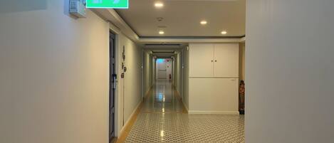 A hallway with patterned flooring, a green emergency exit sign, and a fire extinguisher.