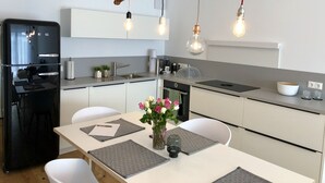 A modern kitchen with a black refrigerator, white cabinets, a dining table with placemats, and a unique hanging light fixture.