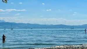 A coastal scene with calm water, boats, and distant mountains under a clear sky.