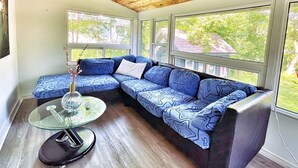 A modern living room with a sectional sofa, a glass coffee table, and large windows offering a view of the outdoors. - Harmonious Cottage by the river (Washago)