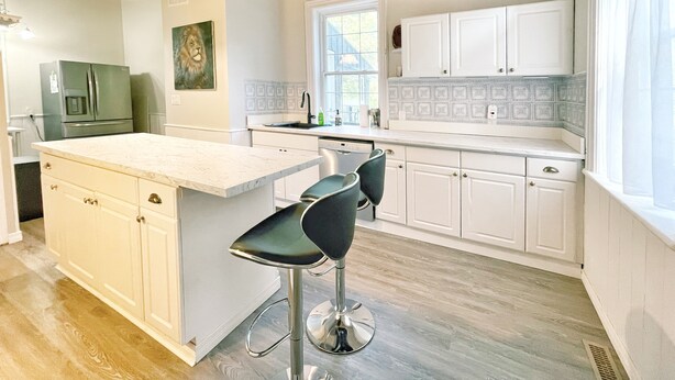 A modern kitchen with white cabinetry, a large island with bar stools, a refrigerator, and pendant lighting. - Harmonious Cottage by the river (Washago)