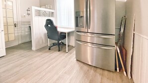 A compact kitchen with a stainless steel refrigerator, a dining table with a chair, and a window with curtains. - Harmonious Cottage by the river (Washago)