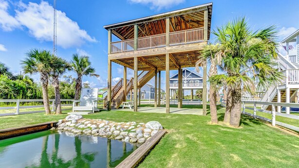 Una terraza de madera con piscina, palmeras y una casa con balcón.