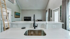 Una cocina moderna con un lavamanos de acero inoxidable, una escalera de madera y un cuadro en la pared.