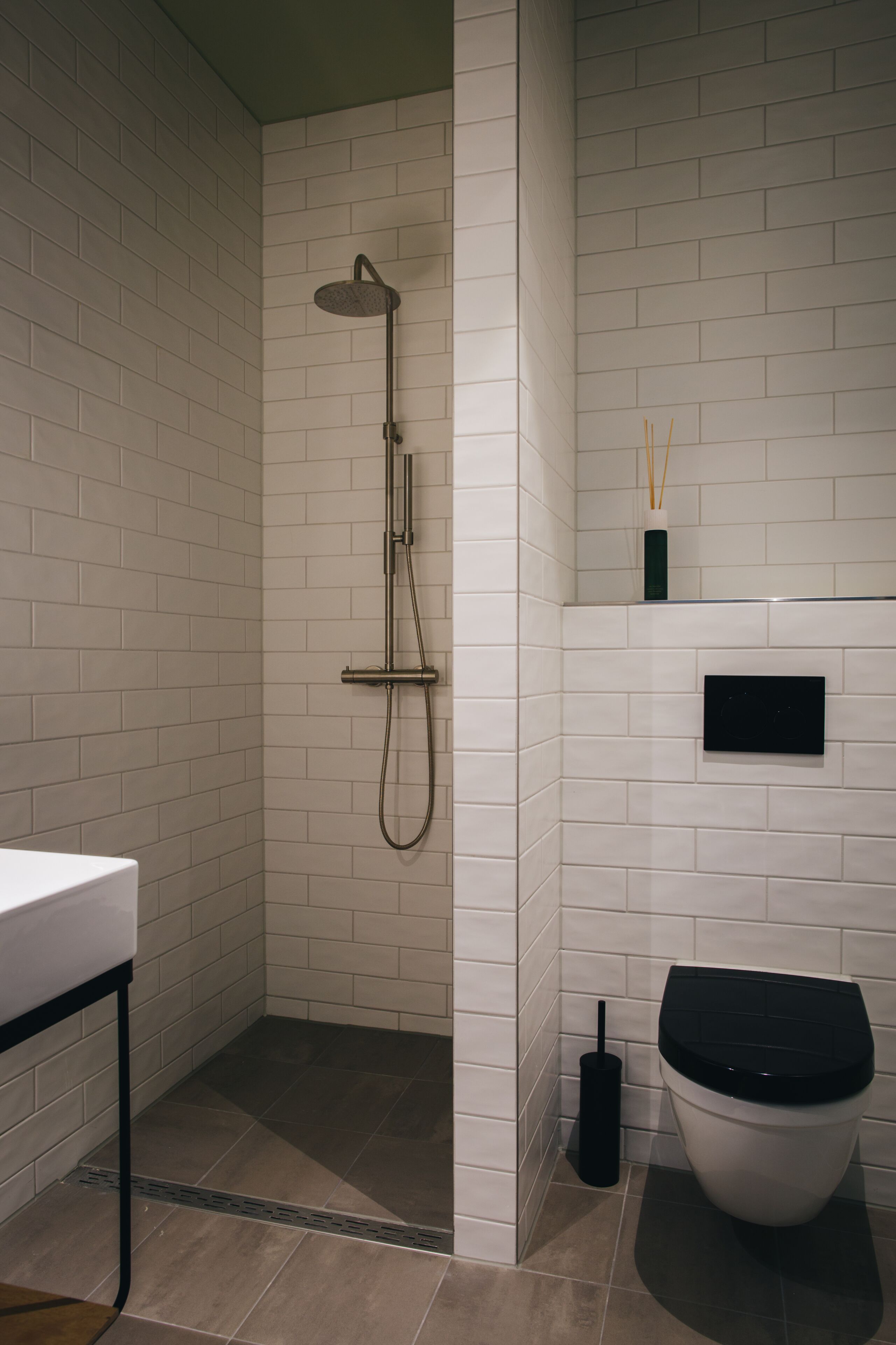 A bathroom with white tiled walls, a shower, a toilet, and a sink.