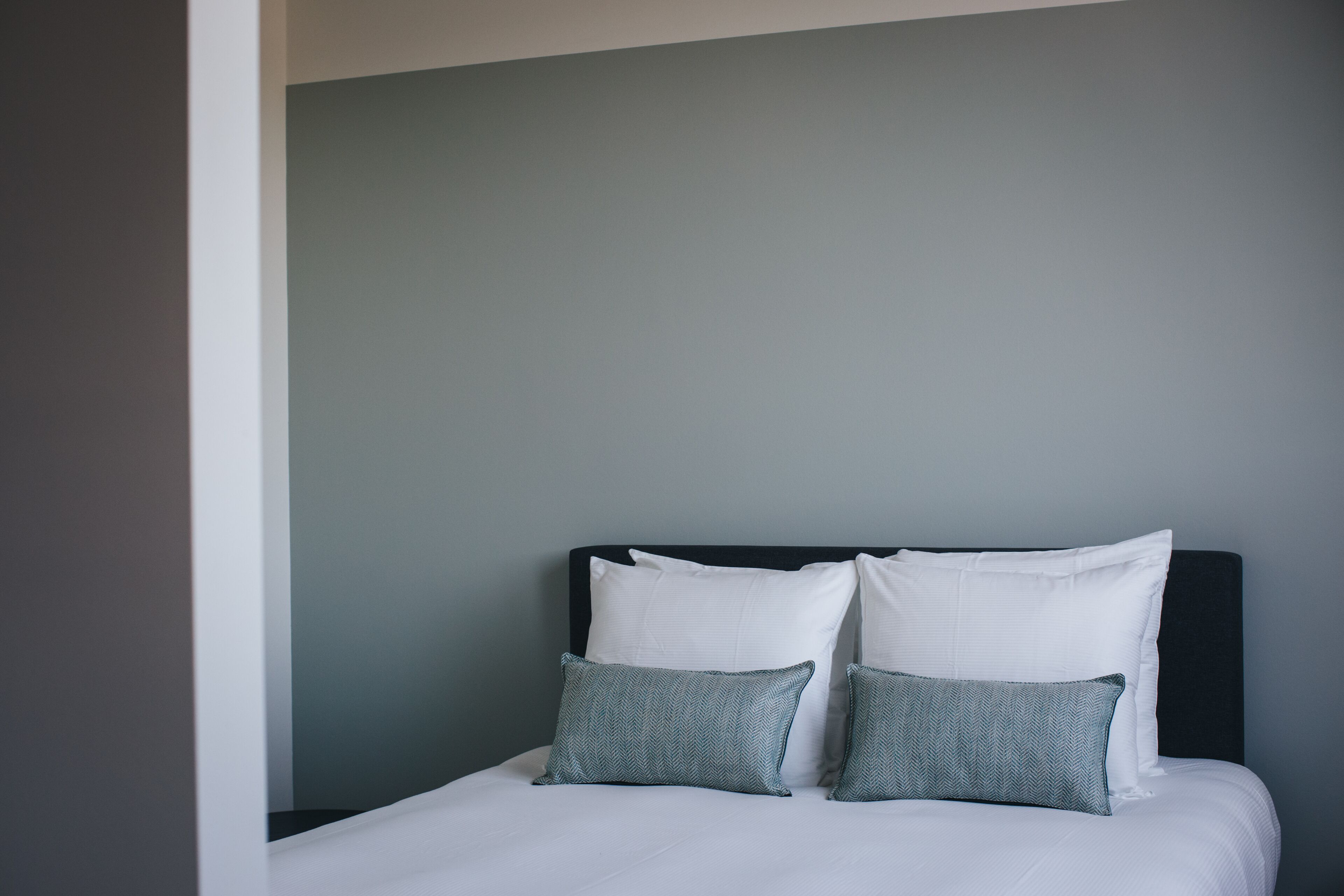 A neatly made bed with white bedding and two grey pillows against a grey wall.