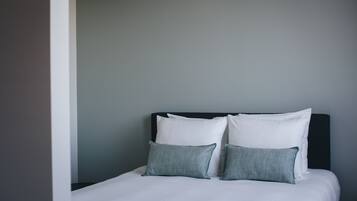 A neatly made bed with white bedding and two grey pillows against a grey wall.