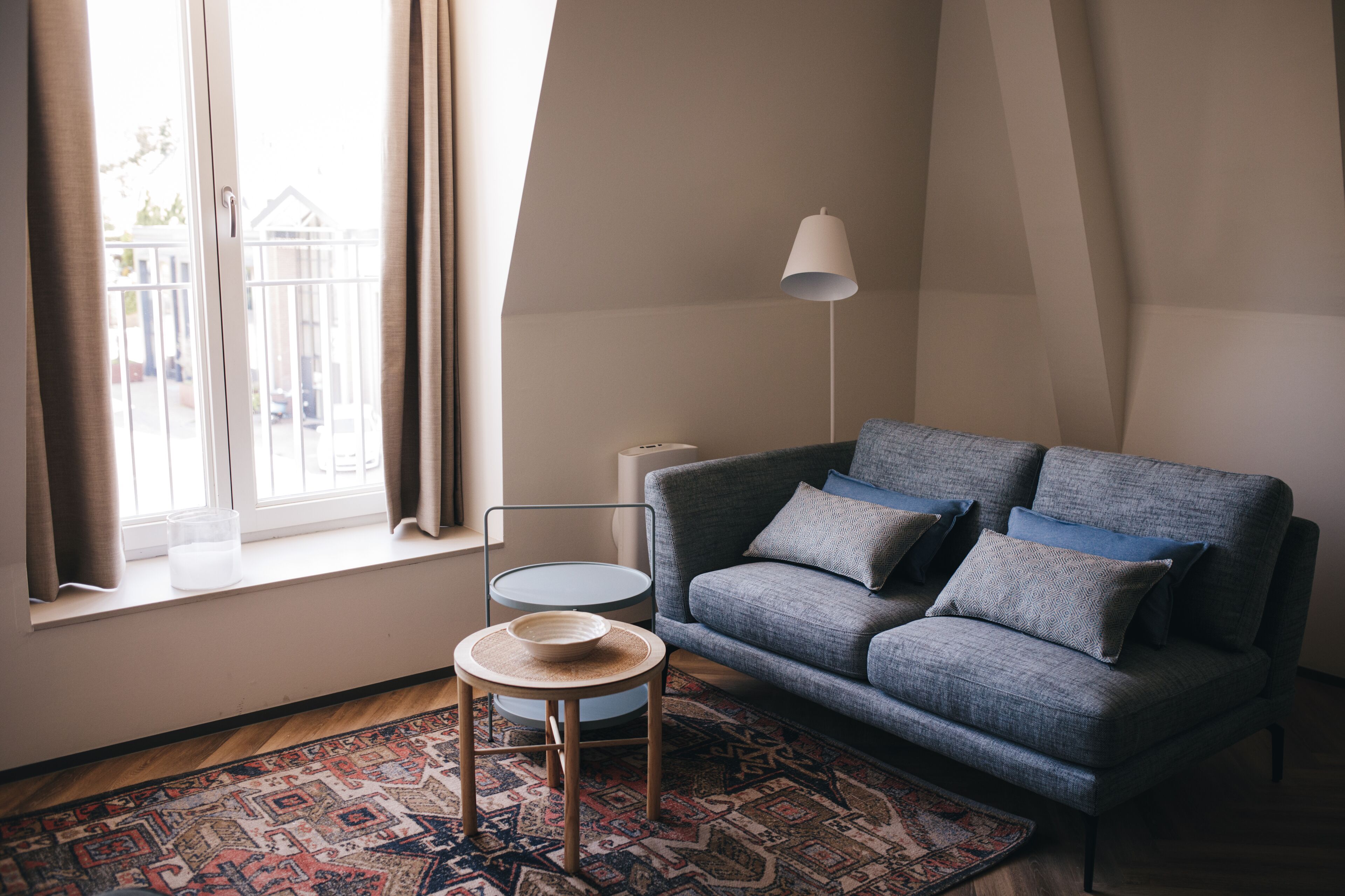 A living room with a grey sofa, a small round table, a floor lamp, and a patterned rug.