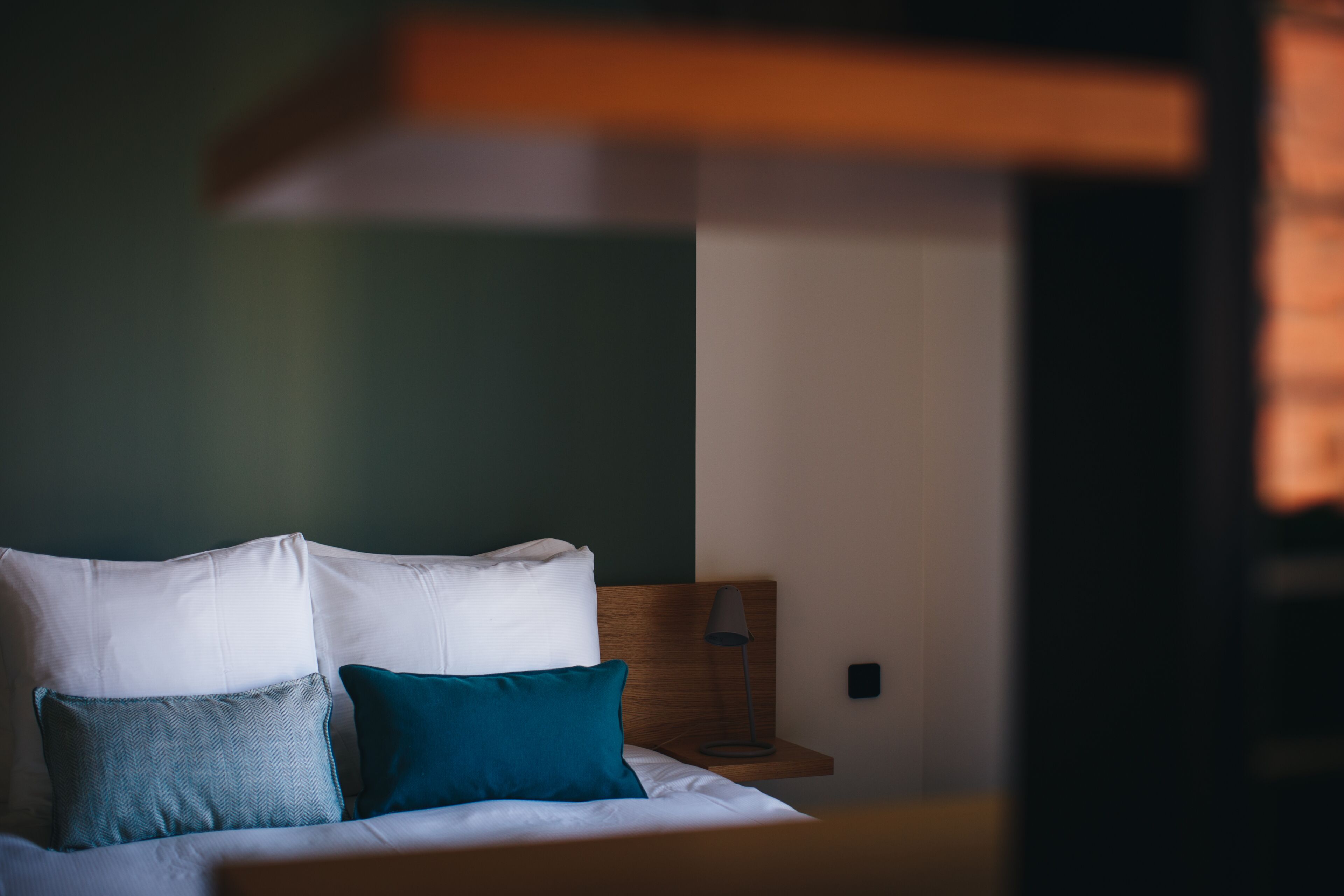 Una cama con almohadillas blancas y azul turquesa, un cabecero de madera y una mesita de noche con lámpara.