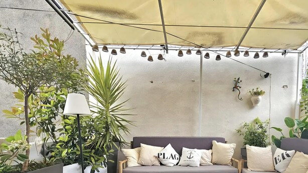 A cozy outdoor seating area with a wooden table, a sofa with cushions, and potted plants.