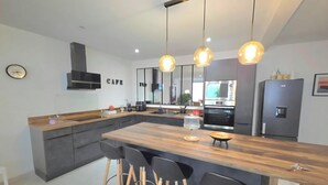 A modern kitchen with a central island, pendant lights, a built-in oven, and a refrigerator.