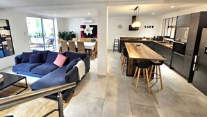 A modern living room with a sofa, dining area, kitchen, and large windows.