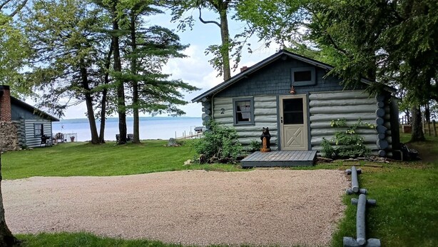 A log cabin with a gravel driveway and a bear statue in front. - Waterfront Modernized Rustic Log Cabin on Indian Lake, Manistique, MI (Manistique)
