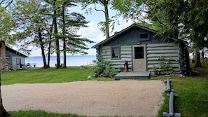 A log cabin with a gravel driveway and a bear statue in front. - Waterfront Modernized Rustic Log Cabin on Indian Lake, Manistique, MI (Manistique)