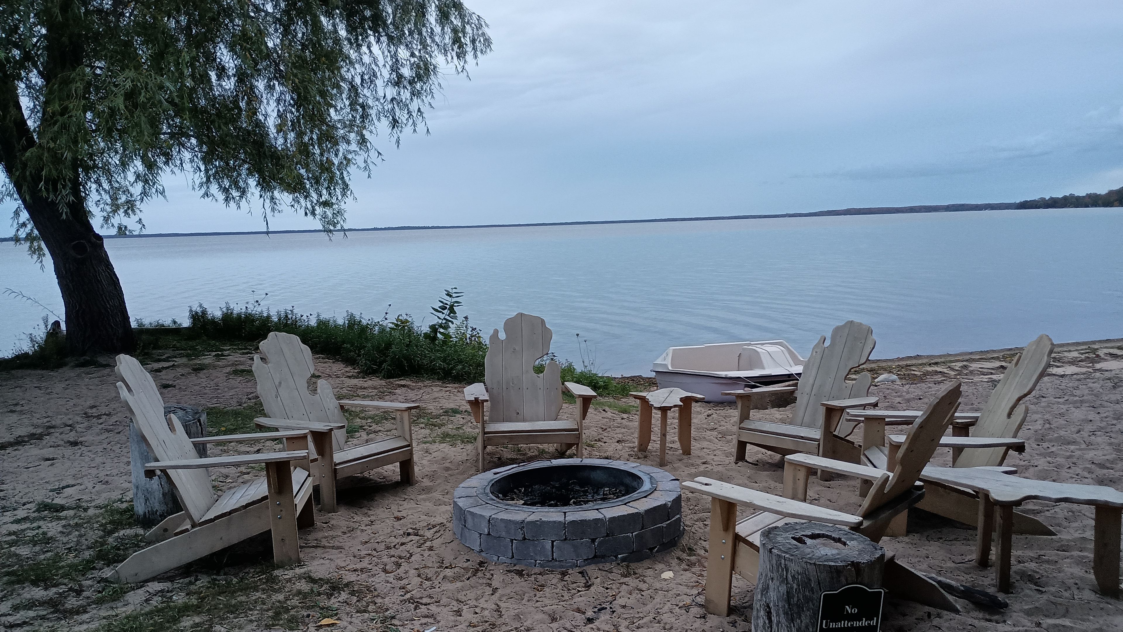 A lakeside seating area with Adirondack chairs and a fire pit.