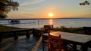 A wooden deck with a table and chairs overlooking a lake at sunset. - Waterfront Modernized Rustic Log Cabin on Indian Lake, Manistique, MI (Manistique)