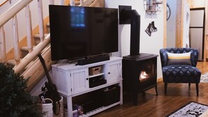 Un soggiorno con una TV su un mobile bianco, un camino a legna nero, una poltrona blu con motivo decorativo e una scala in legno.