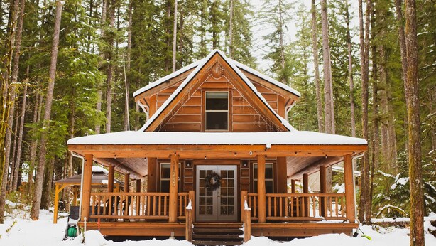Una baita di legno con veranda, circondata da alberi alti e coperta di neve.