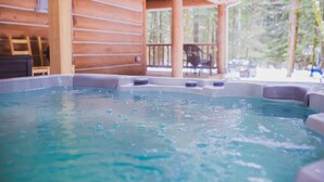 Una vasca idromassaggio in una baita di legno con un patio in legno e sedie.