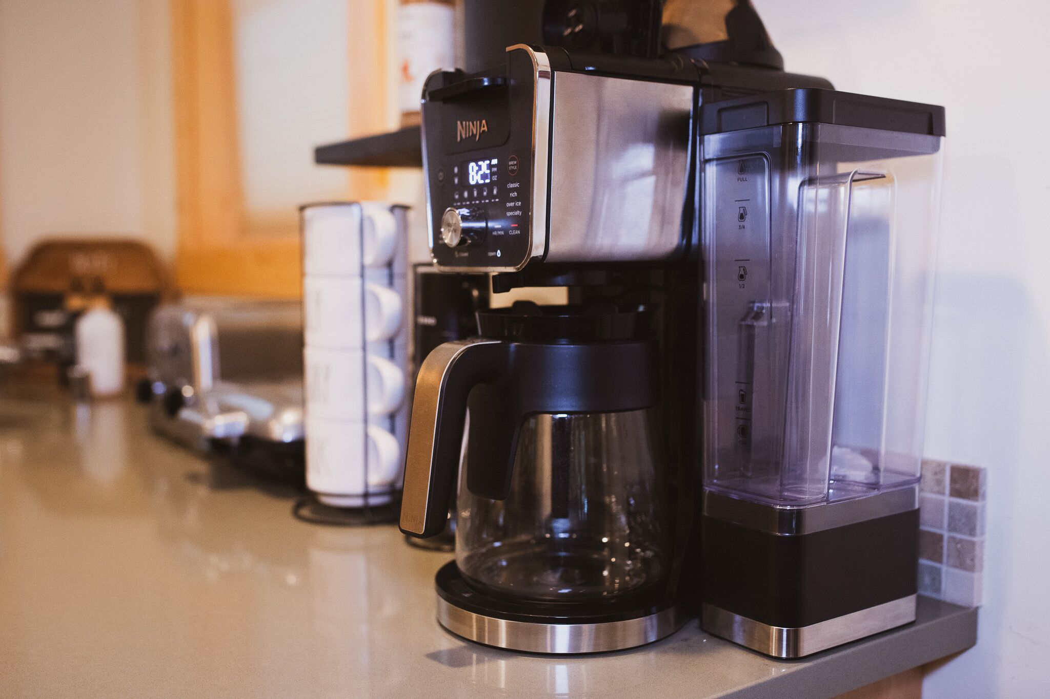 Una cafetera con pantalla digital, jarra de vidrio y depósito de agua transparente.