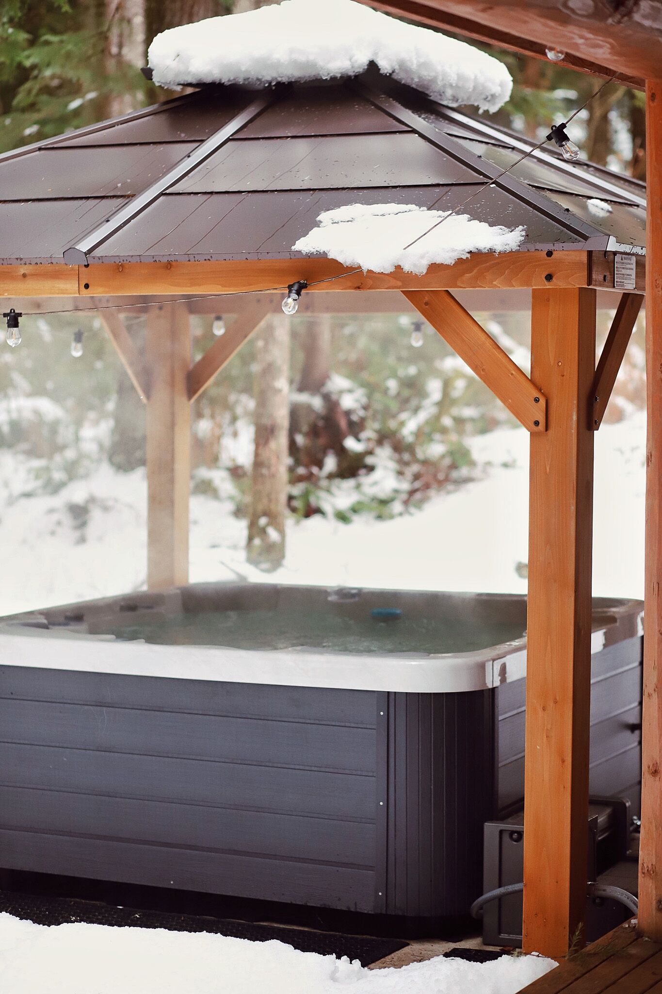 Ein hölzerner Pavillon mit Whirlpool darunter, umgeben von Schnee.