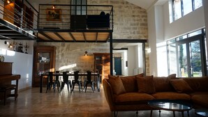 A spacious loft-style living area with a high ceiling, a built-in loft bed, a dining area with a wooden table and chairs, and large windows offering views of the outdoors. - Avignon - Mas de la Roule - 18 people - Swimming pool - Park 2 ha (Avignon)