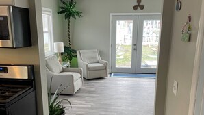 Eine moderne Küche mit integriertem Mikrowellenherd und Herd, ein Essbereich mit weißem Sofa und einer Topfpflanze, sowie der Blick auf eine Wohngegend durch eine Glastür.
