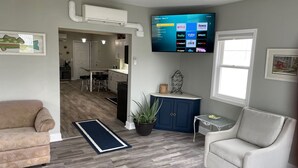 Ein Wohnzimmer mit Flachbildfernseher an der Wand, einer Couch, einem gemusterten Sessel, einem Blumentopf und einem kleinen Tisch mit einer Dekoration.