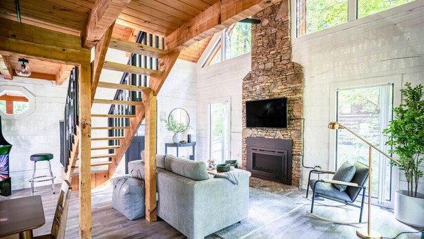 Un vaste salon doté d’une cheminée en pierre, d’un grand téléviseur et d’un escalier en bois.