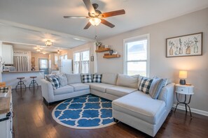 A modern living room with a sectional sofa, a ceiling fan, and a kitchen area in the background. - Cozy Convenient Cottage (Alcoa)