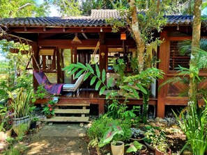 Una casa di legno con veranda, un'amaca e diverse piante in vaso.