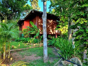 Una baita di legno con tetto di paglia, immersa nel verde e circondata da un giardino.